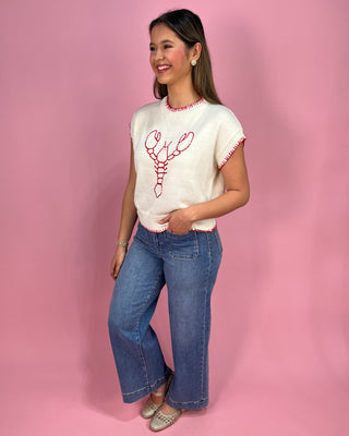 Woman wearing a white top with red lobster design and blue jeans on a pink background
