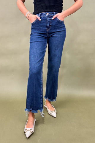 Person wearing blue jeans with a frayed hem on a plain background