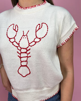 White sweater with red lobster design on a pink background
