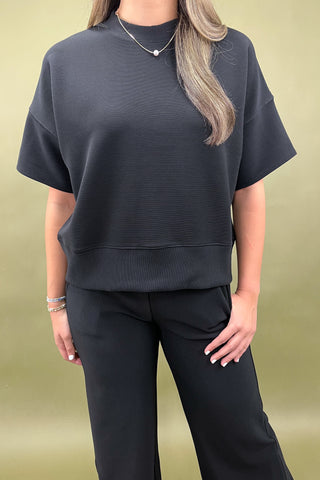 Person wearing a dark gray top and black pants on a beige background