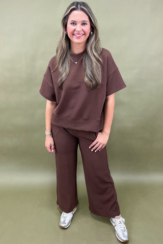 Woman wearing a brown outfit with white sneakers against a green background