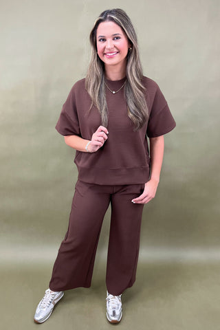 Woman wearing a brown outfit with white sneakers on a beige background