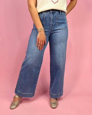 Person wearing blue jeans and a white top with a pink background