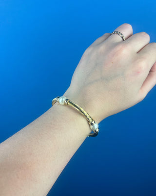 Shop the Gold & Pearl Bangle featuring a twisted gold-tone design, faux pearl accents, and a secure hinged closure for timeless elegance.