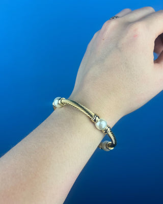 Shop the Gold & Pearl Bangle featuring a twisted gold-tone design, faux pearl accents, and a secure hinged closure for timeless elegance.