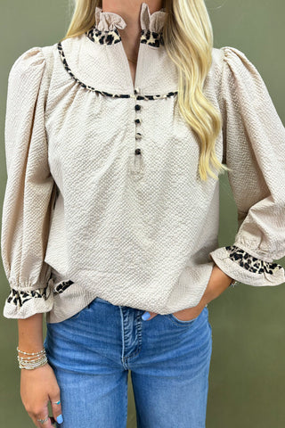 Woman wearing a beige blouse with floral embroidery and blue jeans against a green background