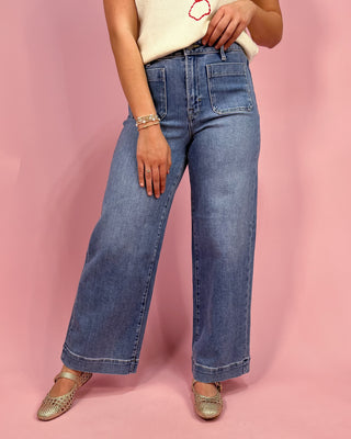 Person wearing blue jeans and a white top with a pink design on a pink background