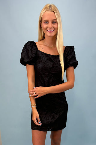 Woman wearing a black dress with puff sleeves against a light blue background