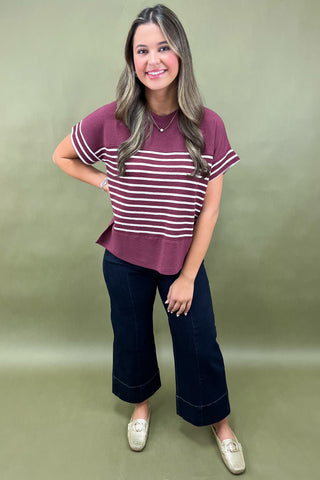 Woman wearing a maroon and white striped shirt with dark jeans on a green background