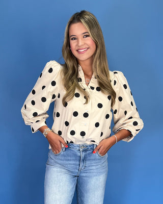 Woman wearing a polka dot blouse and jeans against a blue background