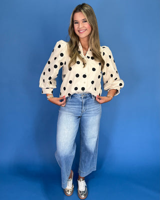 Woman wearing a polka dot blouse and jeans against a blue background
