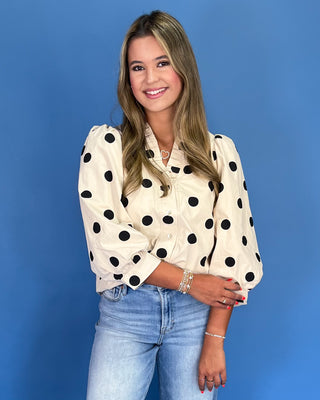 Woman wearing a polka dot blouse and jeans against a blue background