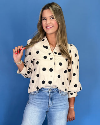 Woman wearing a polka dot blouse and jeans against a blue background