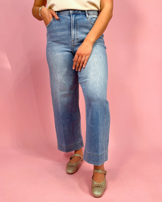 Person wearing blue jeans and sandals on a pink background