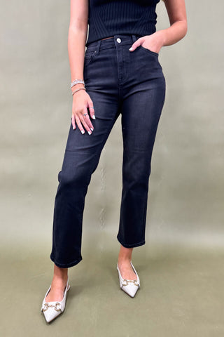 Person wearing dark blue jeans and white shoes on a plain background