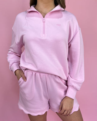 Person wearing a pink fleece outfit with a quarter-zip top and shorts on a pink background