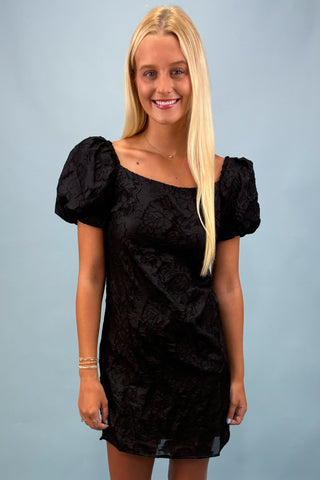 Woman wearing a black dress with puff sleeves against a light blue background