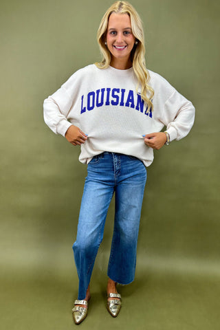Woman wearing a white sweatshirt with 'LOUISIANA' printed on it against a green background