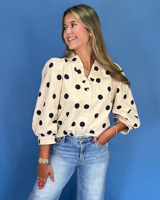 Woman wearing a polka dot blouse and jeans against a blue background