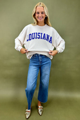 Woman wearing a white sweatshirt with 'LOUISIANA' printed on it against a green background