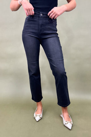 Person wearing dark blue jeans and white shoes on a plain background