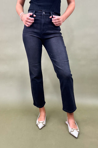 Person wearing dark blue jeans and white shoes on a plain background