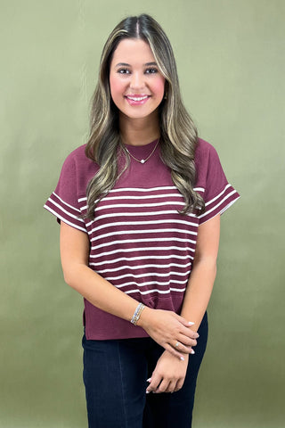 Woman wearing a maroon and white striped shirt against a green background
