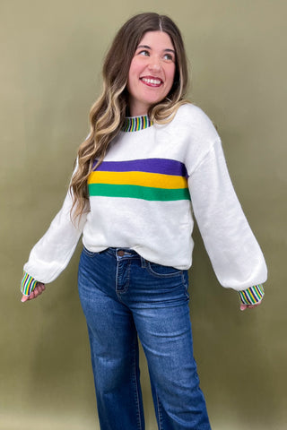 Woman wearing a white sweater with colorful stripes against a beige background