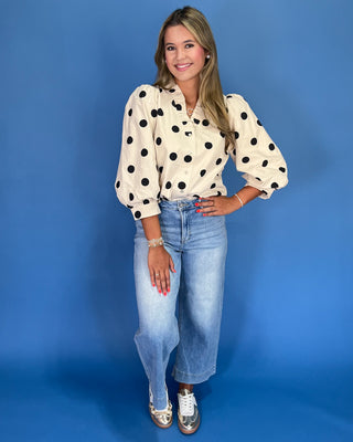 Woman wearing a polka dot blouse and jeans against a blue background