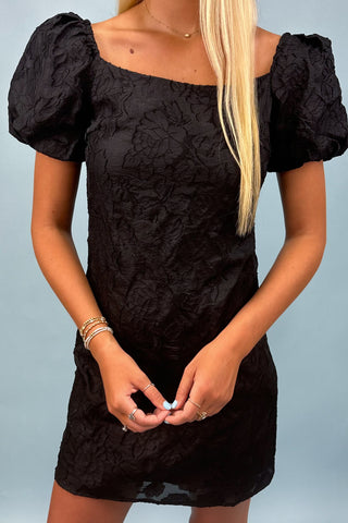 Black dress with puff sleeves worn by a person on a light blue background