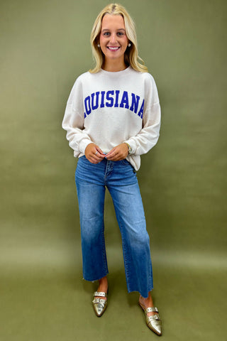 Woman wearing a white sweatshirt with 'LOUISIANA' printed on it against a green background