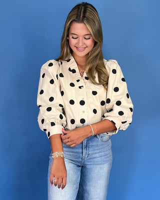 Woman wearing a polka dot blouse and jeans against a blue background