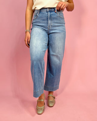Person wearing light blue jeans on a pink background