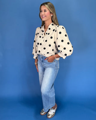 Woman wearing a polka dot blouse and jeans against a blue background