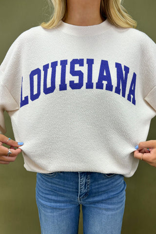 Woman wearing a white sweatshirt with 'LOUISIANA' printed on it against a green background