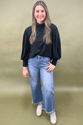 Woman wearing a black top and blue jeans against a green background