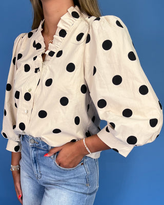 Person wearing a white blouse with black polka dots and blue jeans against a blue background