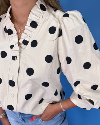 White shirt with black polka dots worn by a person against a blue background