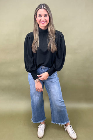 Woman wearing a black top and blue jeans against a green background