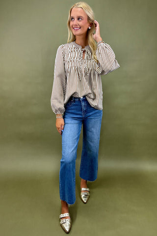 Woman wearing a striped blouse and blue jeans against an olive green background