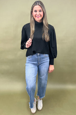 Woman wearing a black top and blue jeans against a green background