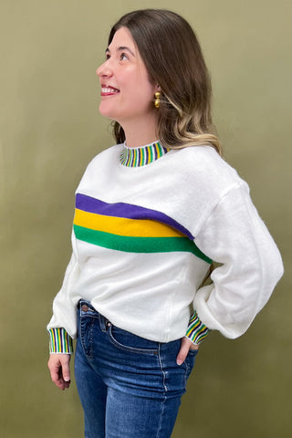 Woman wearing a white sweater with colorful stripes against a green background