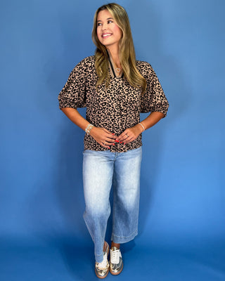 Woman wearing a leopard print top and blue jeans against a blue background