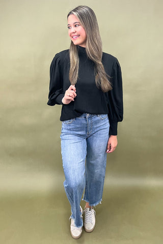 Woman wearing a black top and blue jeans against a green background