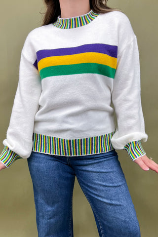 White sweater with colorful stripes worn by a person against a beige background