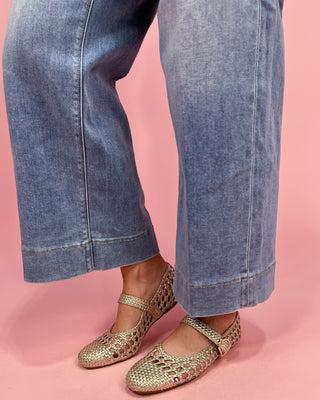 Gold sandals worn with blue jeans on a pink background