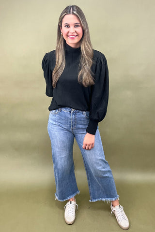 Woman wearing a black top and blue jeans against a green background