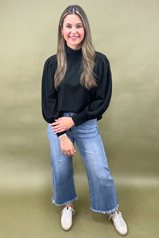Woman wearing a black top and blue jeans against a green background