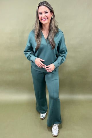 Woman wearing a teal tracksuit against a beige background