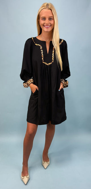 Woman wearing a black dress with gold accents against a light blue background